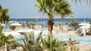 Zona de piscina con palmeras, sombrillas y vistas al mar.