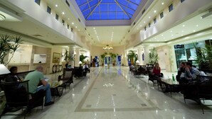 Un amplio vestíbulo de hotel con techo alto y tragaluces, que cuenta con una lámpara central, zonas de estar y suelo pulido.