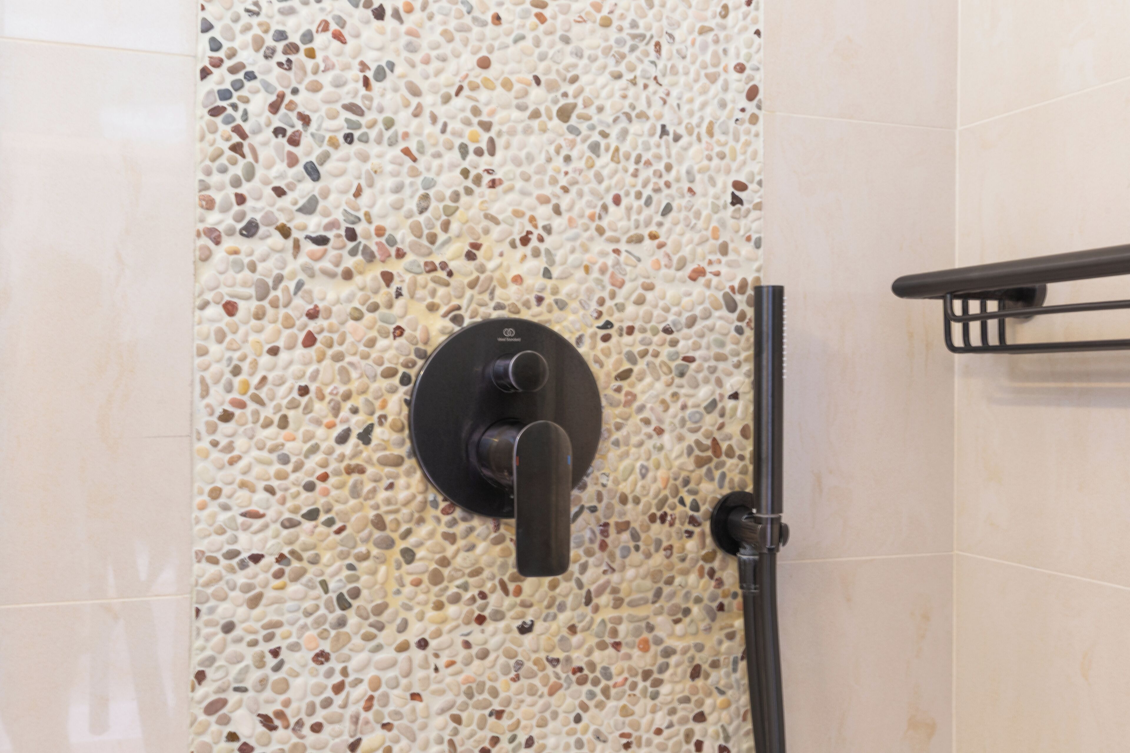A shower with a pebble-patterned wall and a black towel rack.