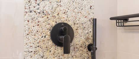 A shower with a pebble-patterned wall and a black towel rack.