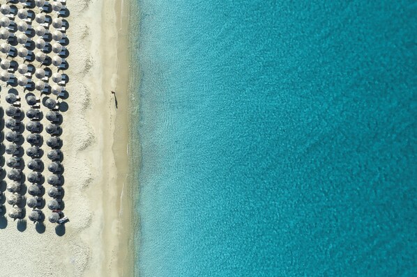 An aerial view of a beach with rows of umbrellas and a clear blue ocean. - Lagos Mare Hotel (Naxos)