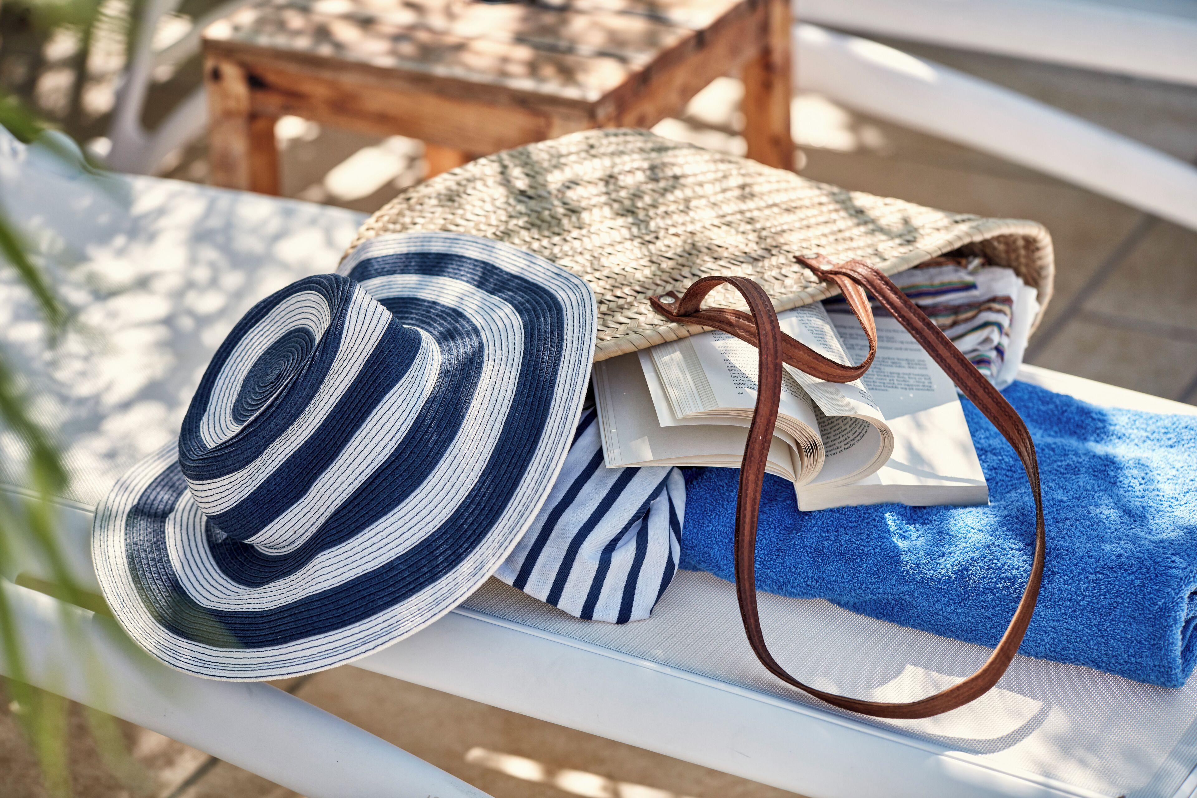 A white bench with a woven bag, a striped hat, and a blue towel.