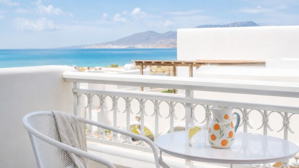 A balcony with a white metal railing, a round table, and a white chair. - Lagos Mare Hotel (Naxos)