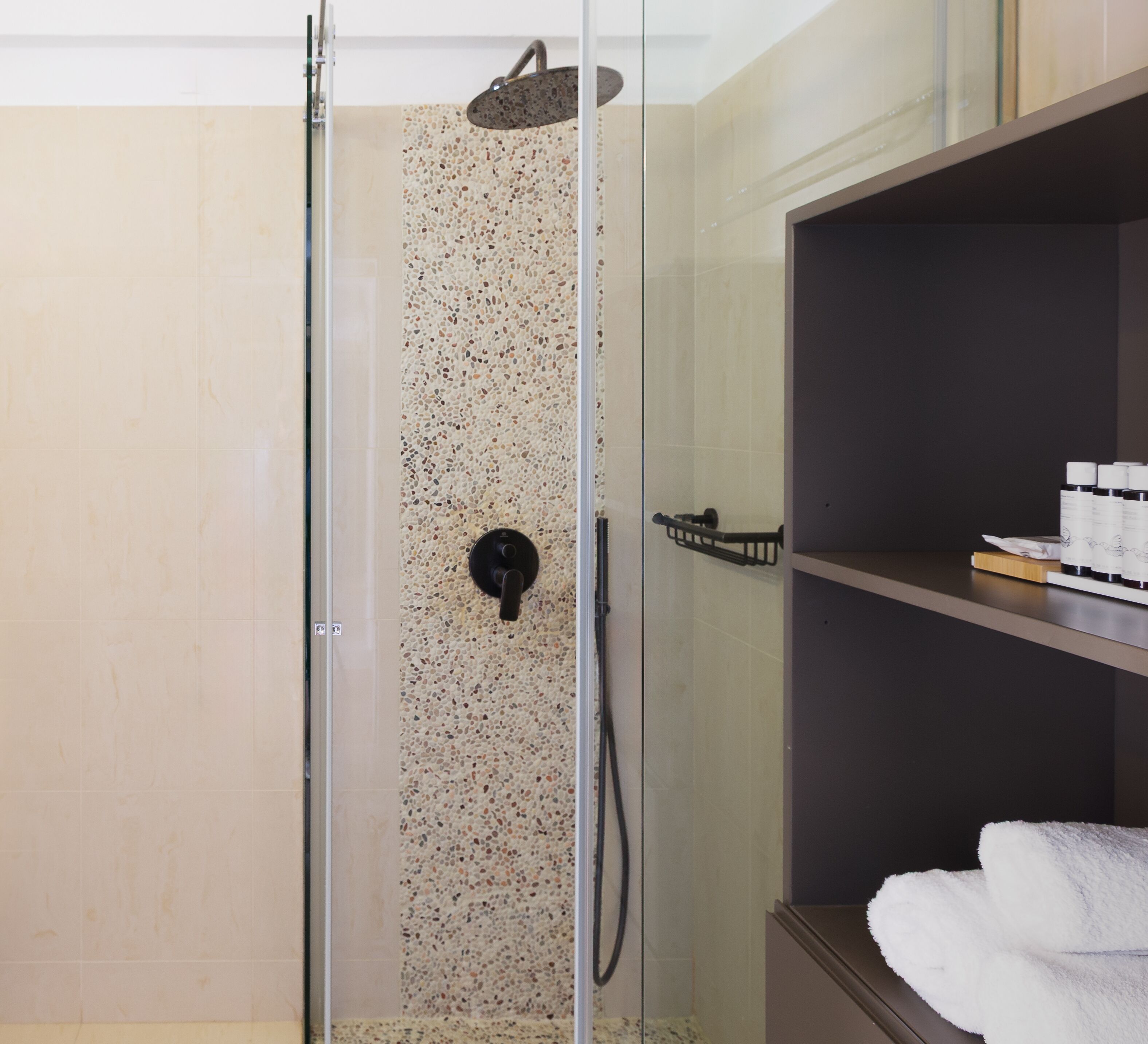 A glass-enclosed shower with a pebble-patterned wall, a control panel, and a towel rack.