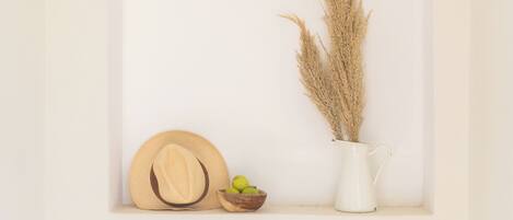 A white arched alcove with a wooden hat, a small bowl, and a white vase with pampas grass.