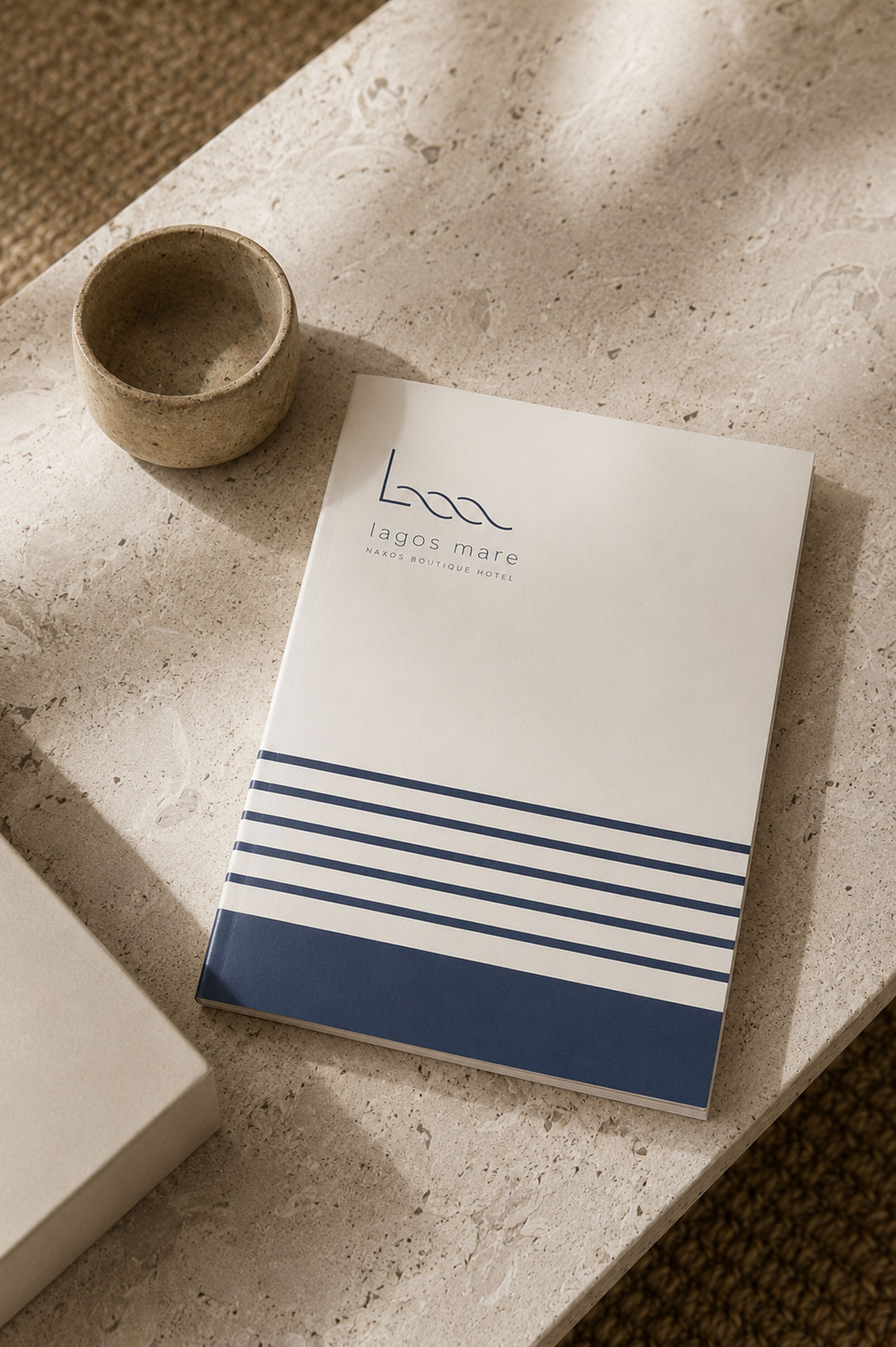 A brochure for the Naxos Boutique Hotel in LAGOS, with a minimalist design and a small cup beside it.