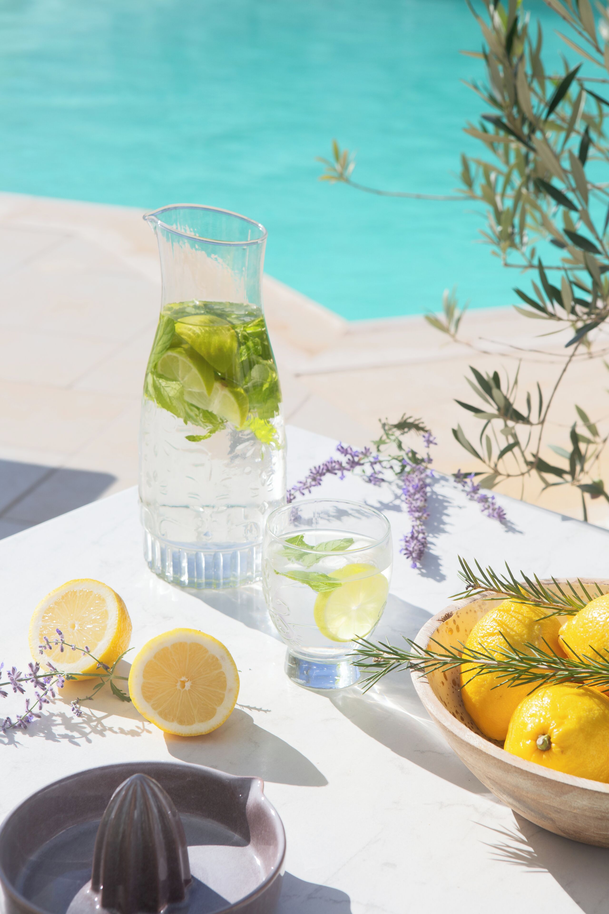 A table with a glass pitcher, a bowl of lemons, and a lemon half.