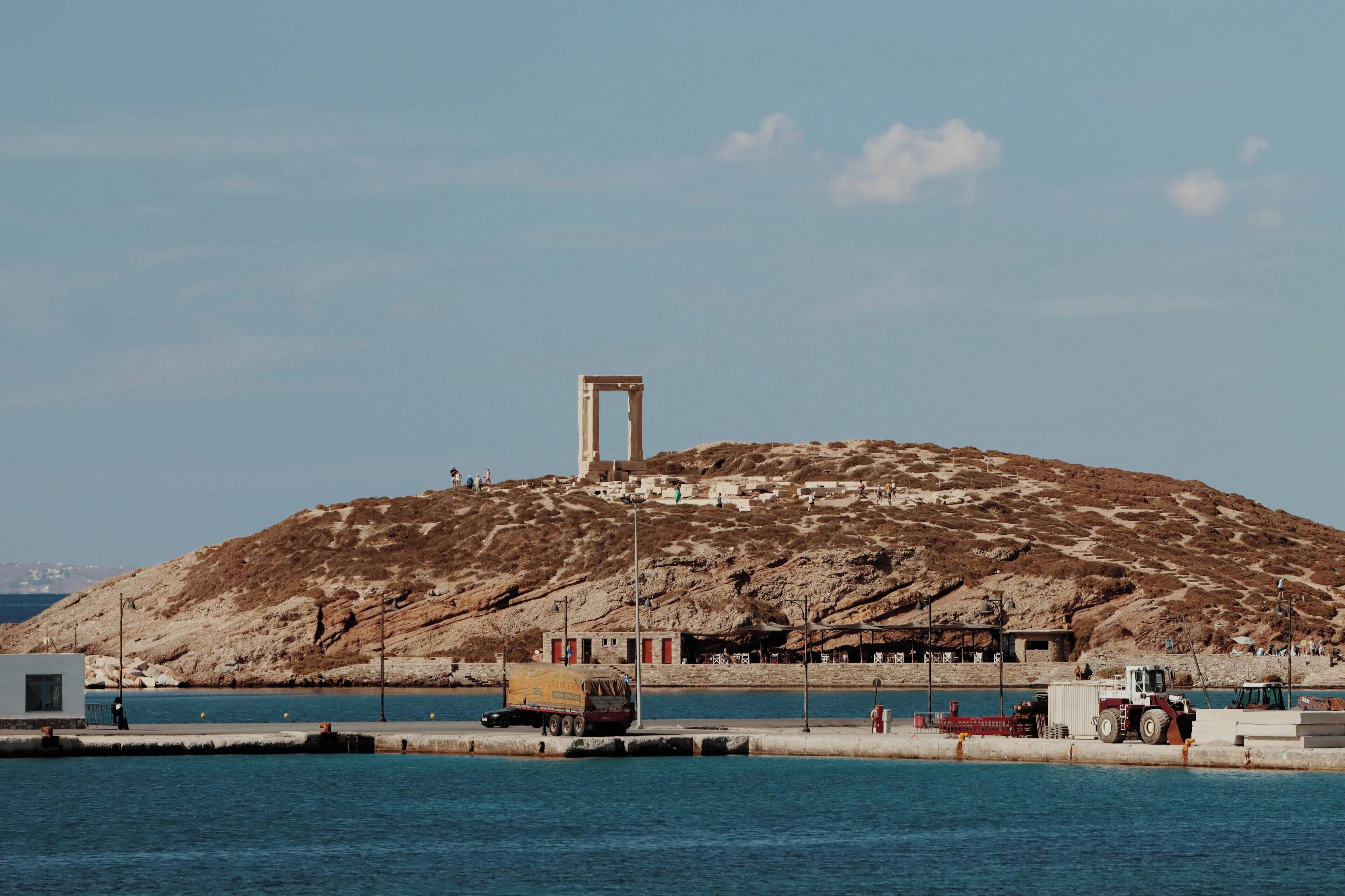 A coastal scene with a rocky hill, a clear sky, and a small building with a prominent doorway.
