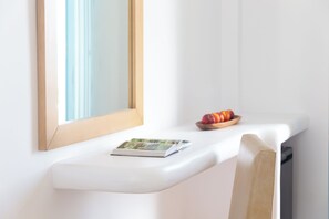 A white bedside table with a book, a bowl of fruit, and a mirror. - Lagos Mare Hotel (Naxos)