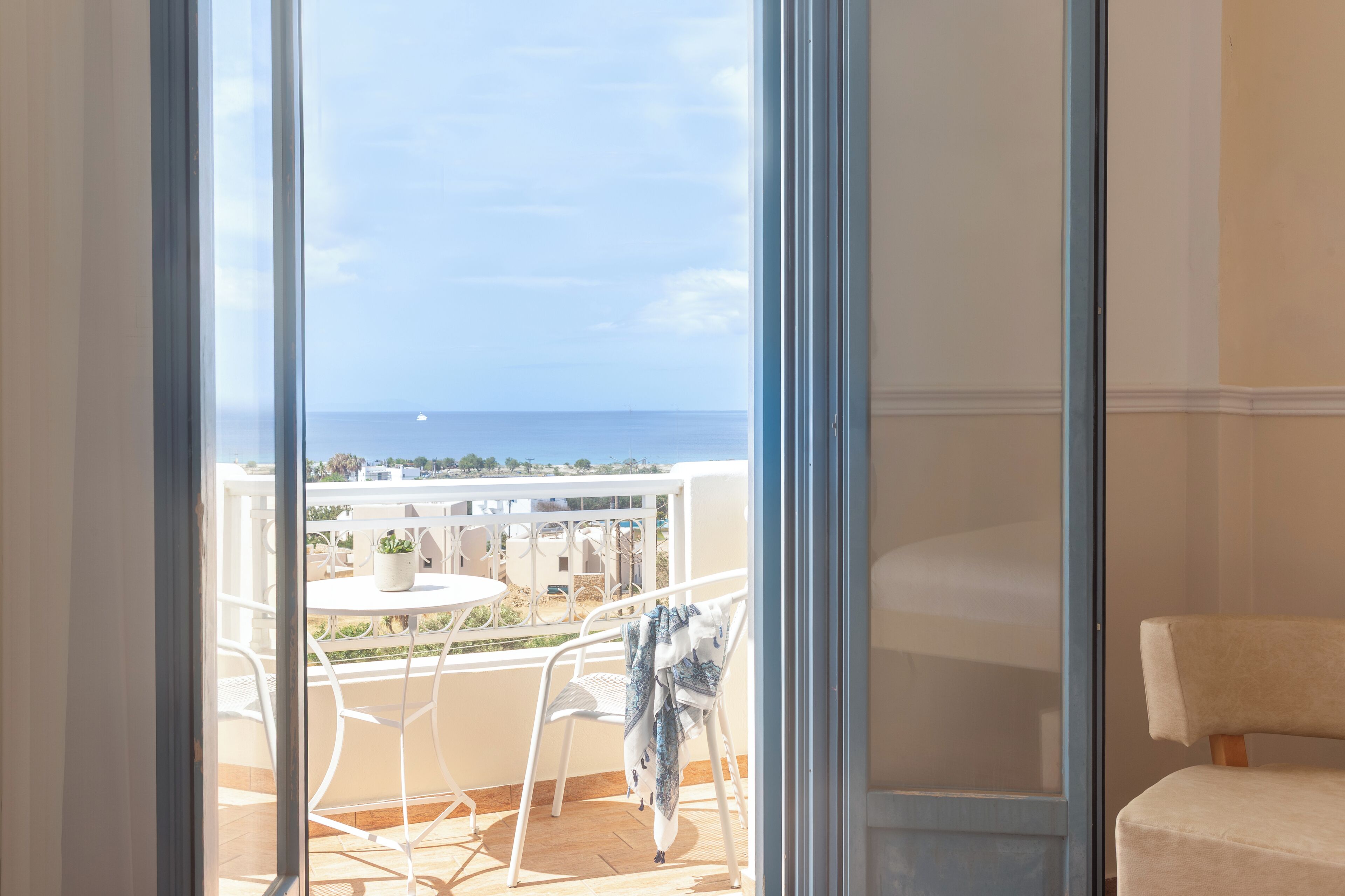 Una habitación con vista al mar, un balcón con mesa y sillas, y una cama.