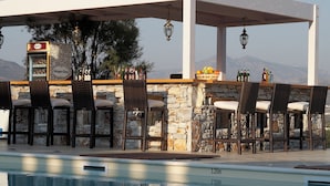 Un bar junto a la piscina con paredes de piedra y sillas de mimbre, una barra de piedra y vistas a las montañas al fondo.