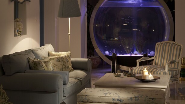 Una sala de estar moderna con un acuario redondo, un sofá, una silla y una mesa con velas.