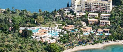 A coastal resort with multiple swimming pools, beachfront villas, and a yacht in the background.