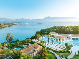 Un resort con una grande piscina, diversi edifici e vista su un lago e montagne.