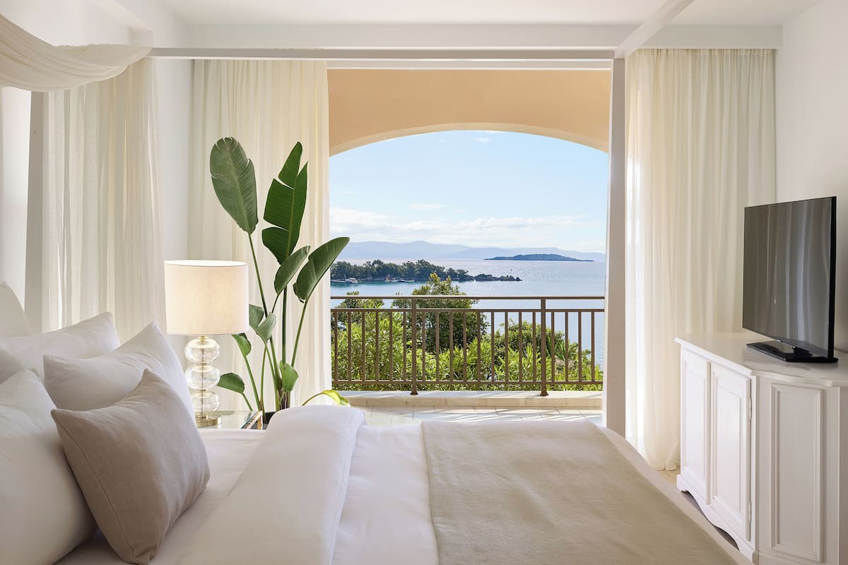Quarto de hotel com uma cama grande, televisão e varanda com vista para o mar.