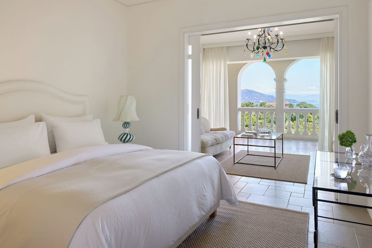 Quarto com uma cama grande, área de estar com mesa e varanda com vista para as colinas.