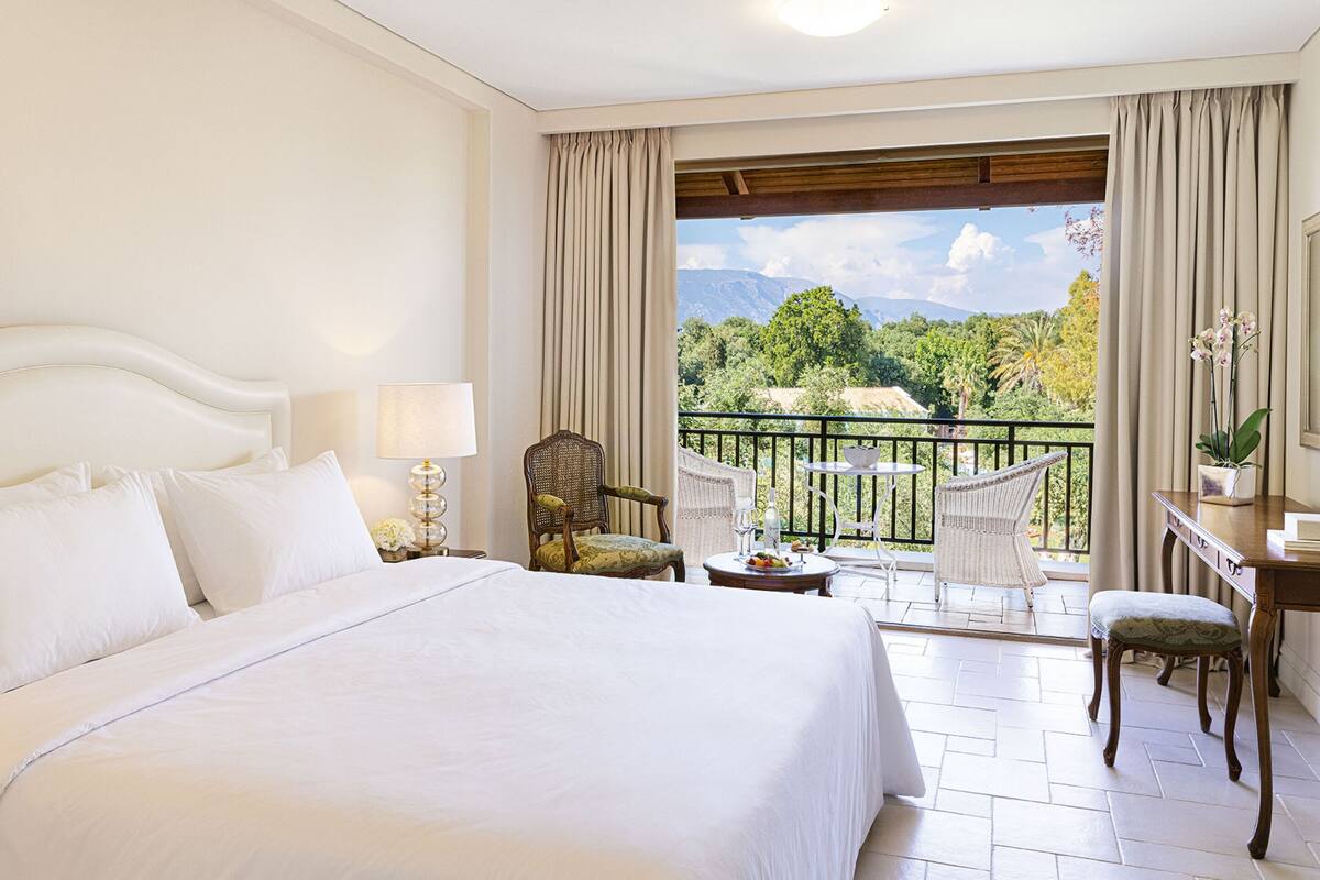 Quarto de hotel com uma cama grande, uma escrivaninha, uma cadeira e varanda com vista para as montanhas.