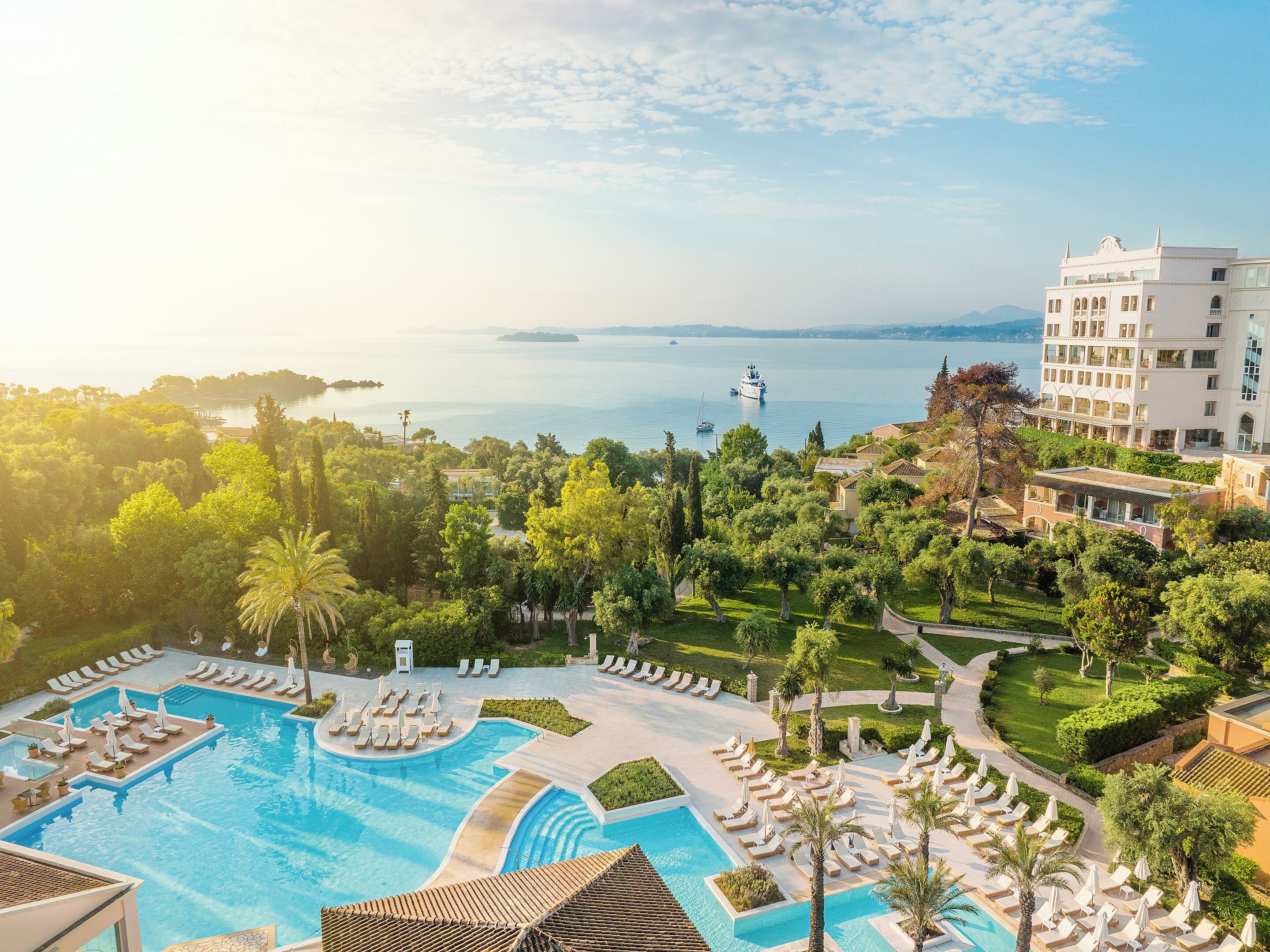 A resort with a large pool, lush greenery, and a view of the sea.
