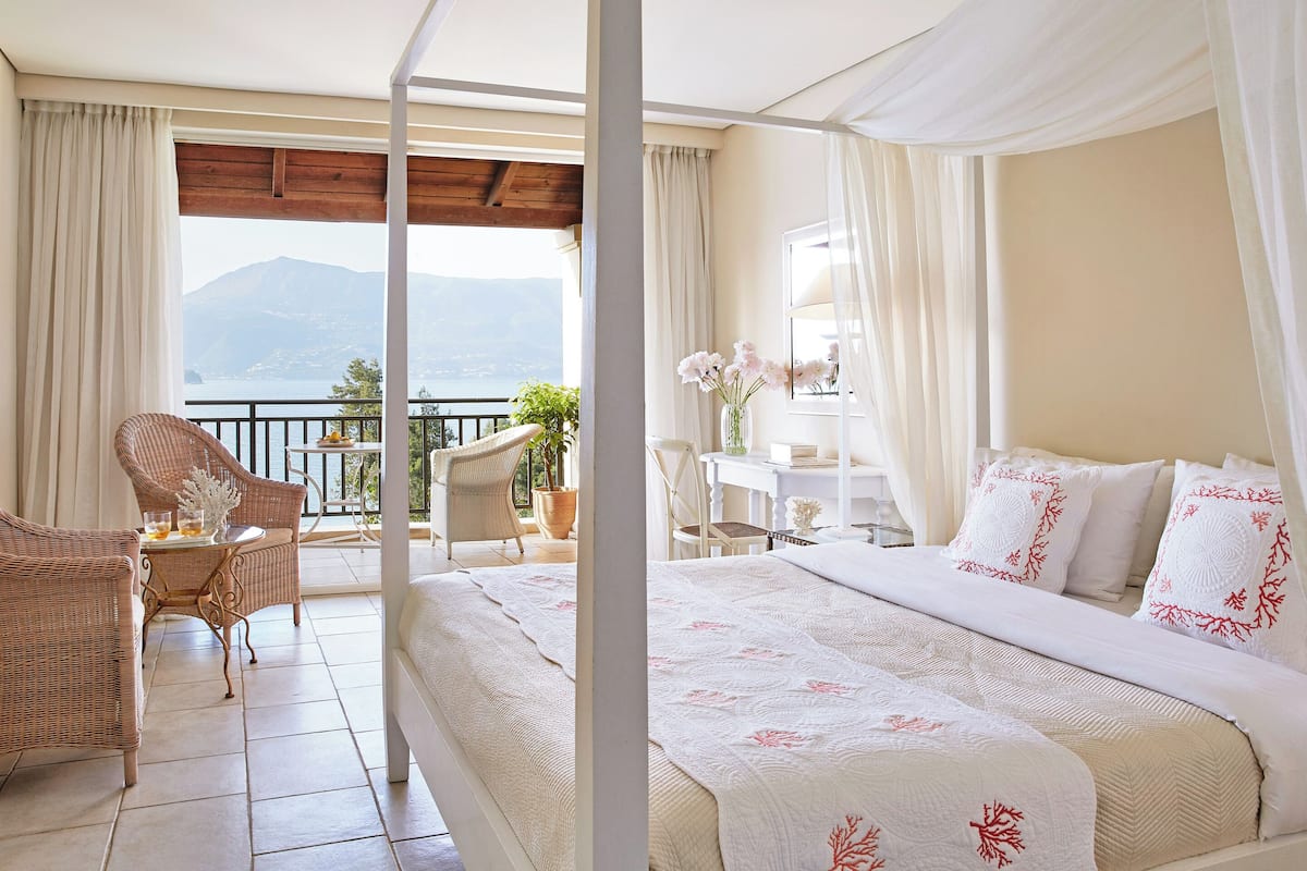Quarto com cama, cadeira, mesa e vista para as montanhas.