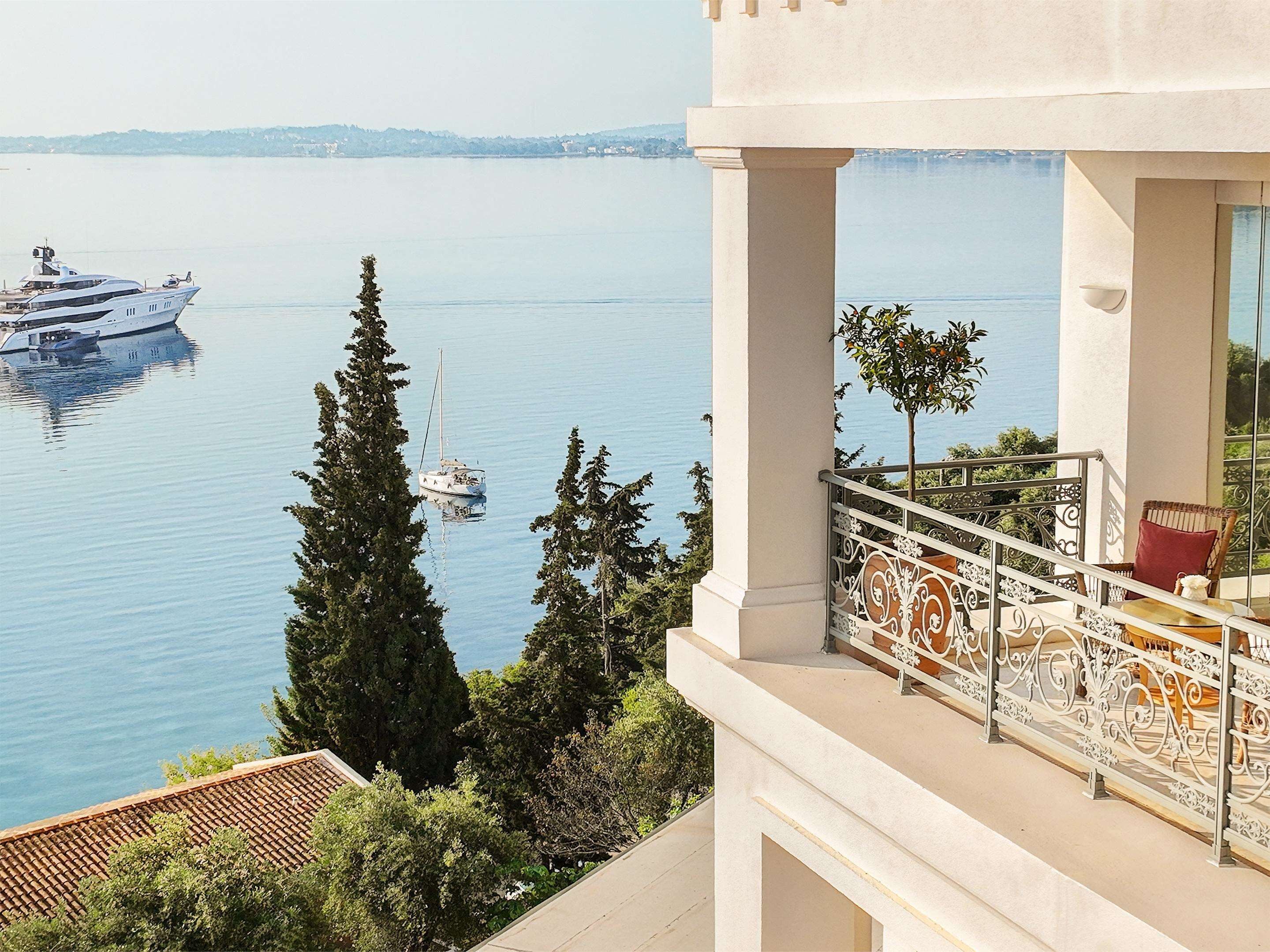 A balcony with a view of a calm lake, a yacht, and a sailboat.