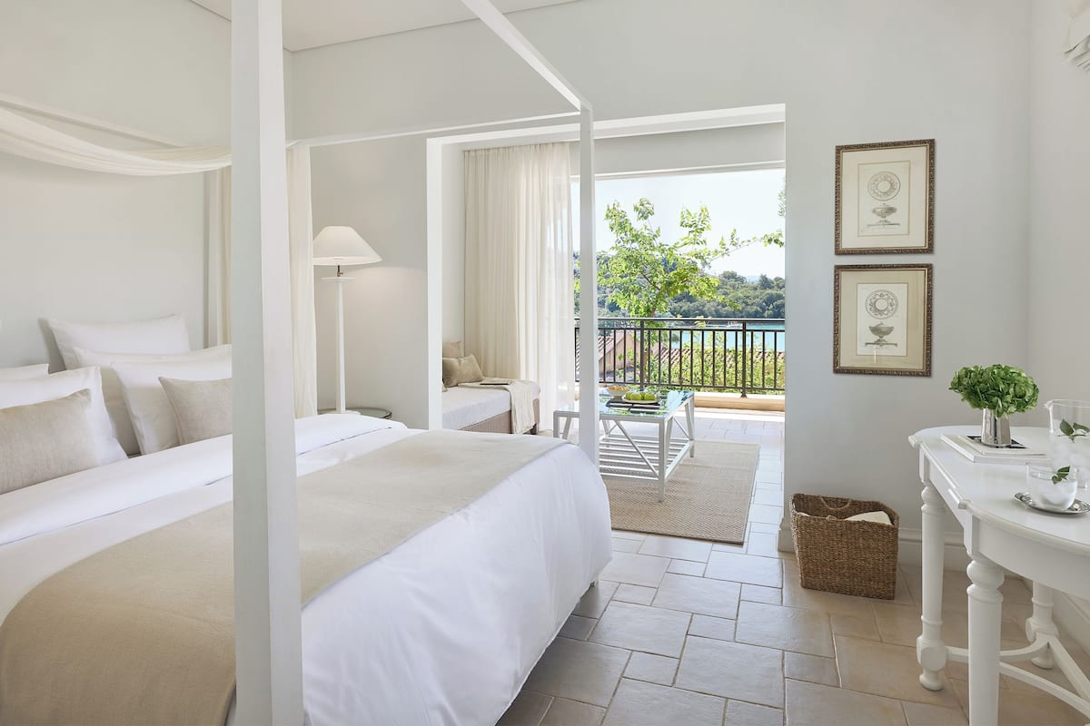 Quarto com duas camas, varanda com vista e uma mesinha com uma planta.