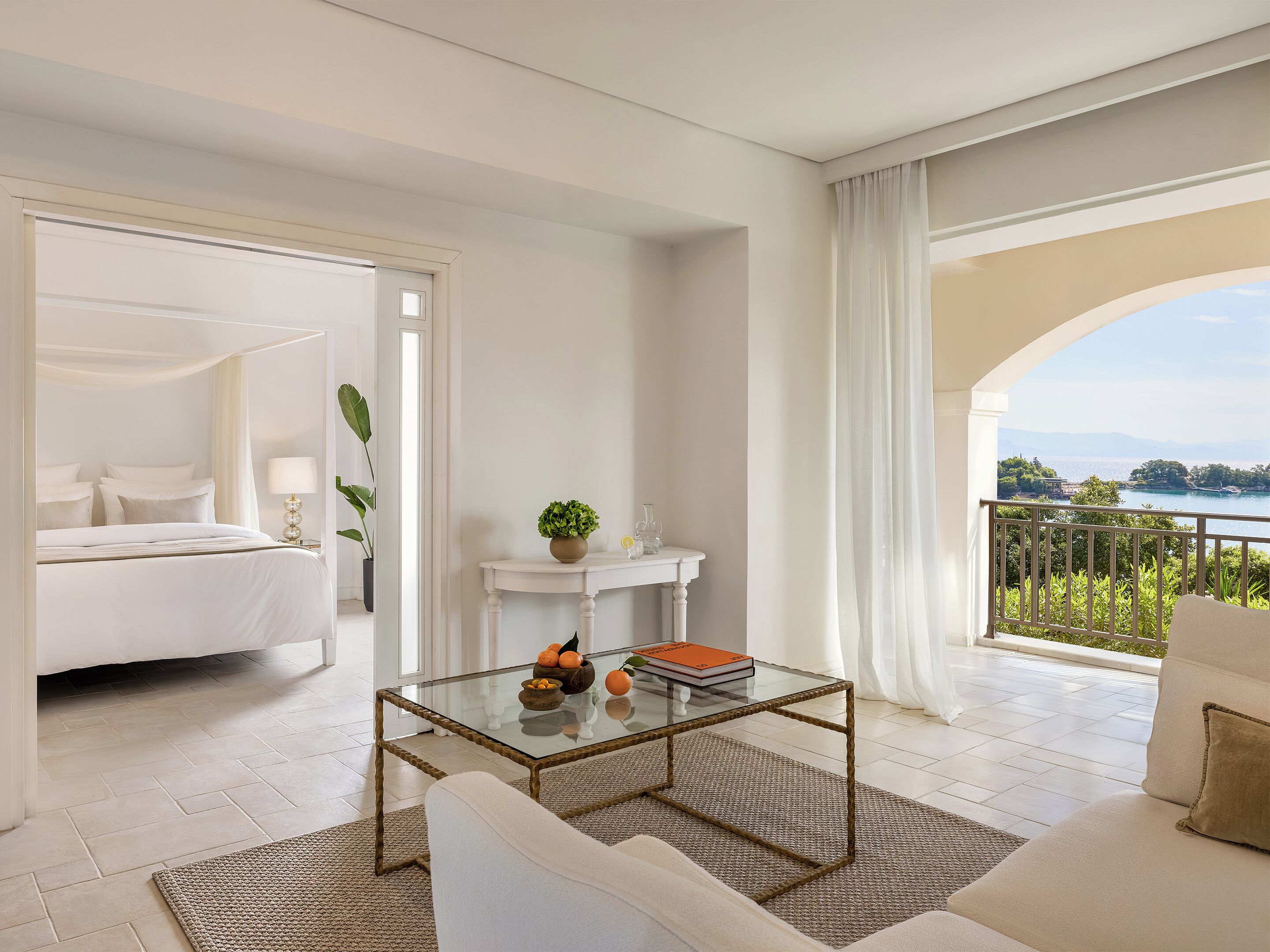 Ein modernes Hotelzimmer mit Bett, Glastisch, Sofa und einem Balkon mit Meerblick.