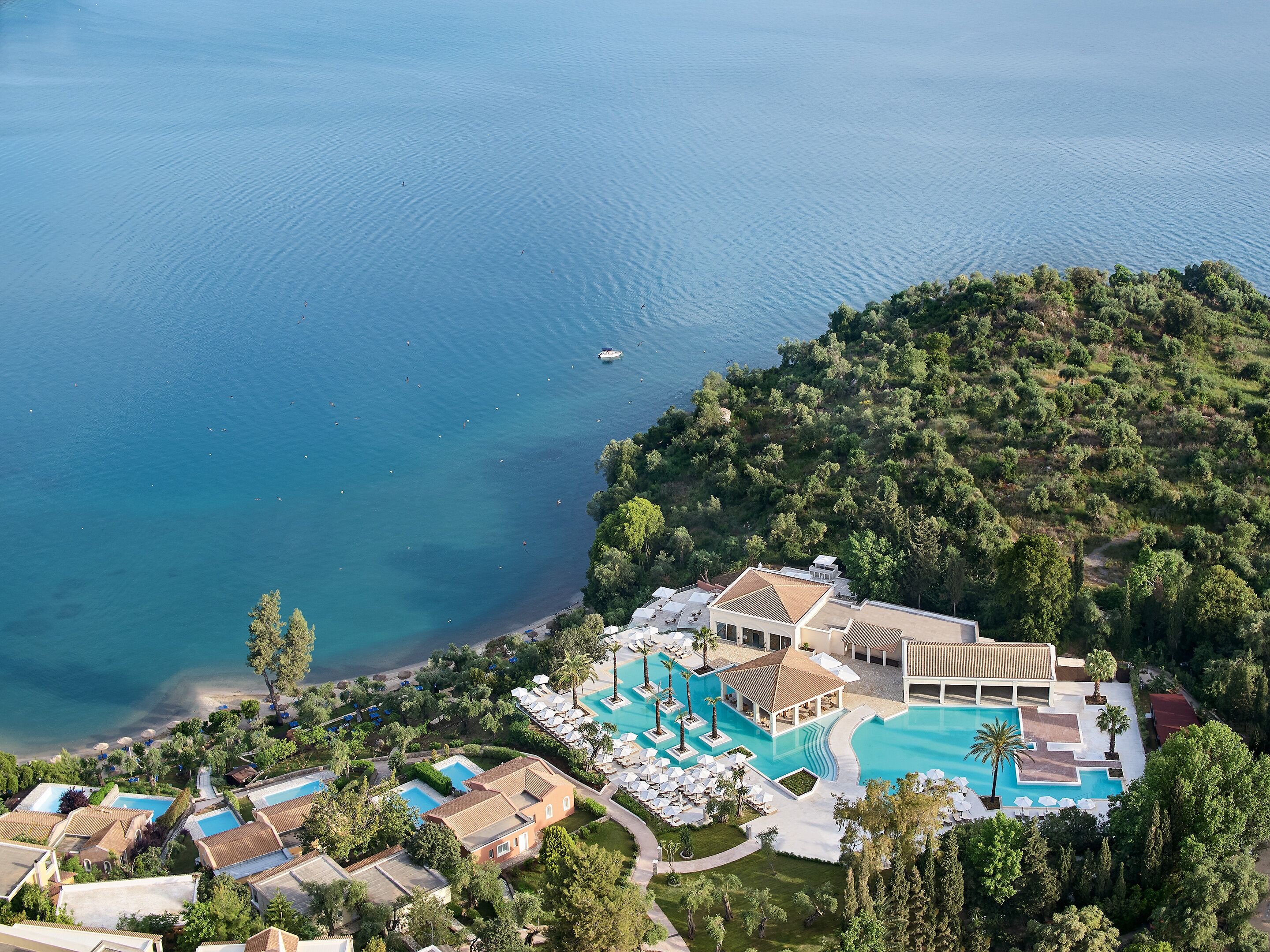 An aerial view of a coastal resort with multiple swimming pools, a beach, and lush greenery.