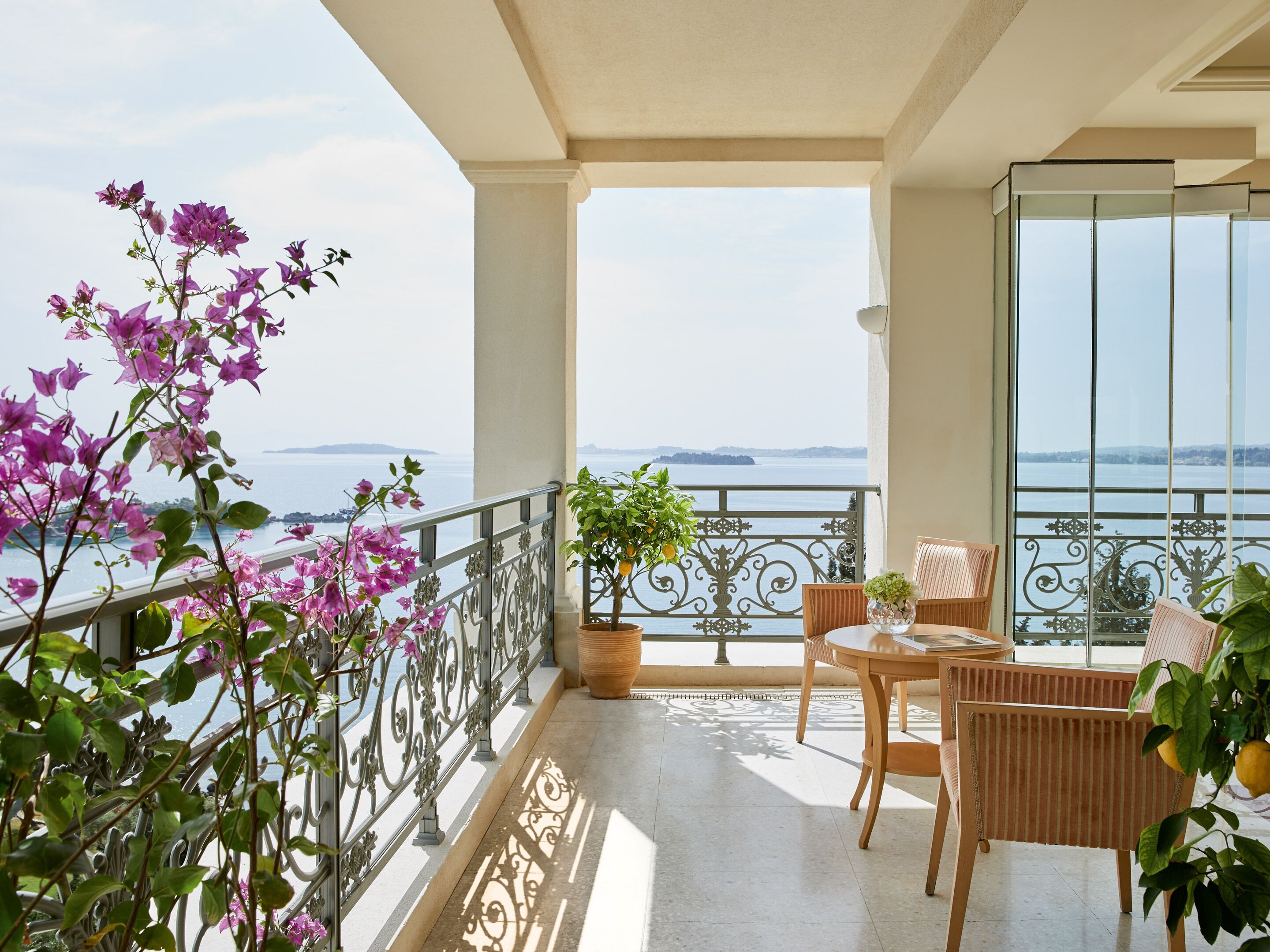 Un balcon avec vue sur la mer, une table avec des chaises et des plantes en pot.