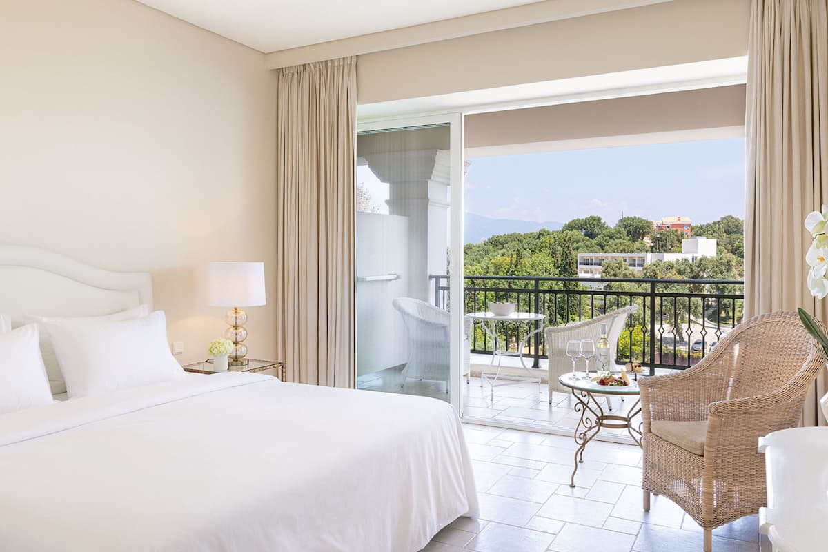 Quarto de hotel com uma cama grande, varanda com móveis de vime e vista para a cidade.