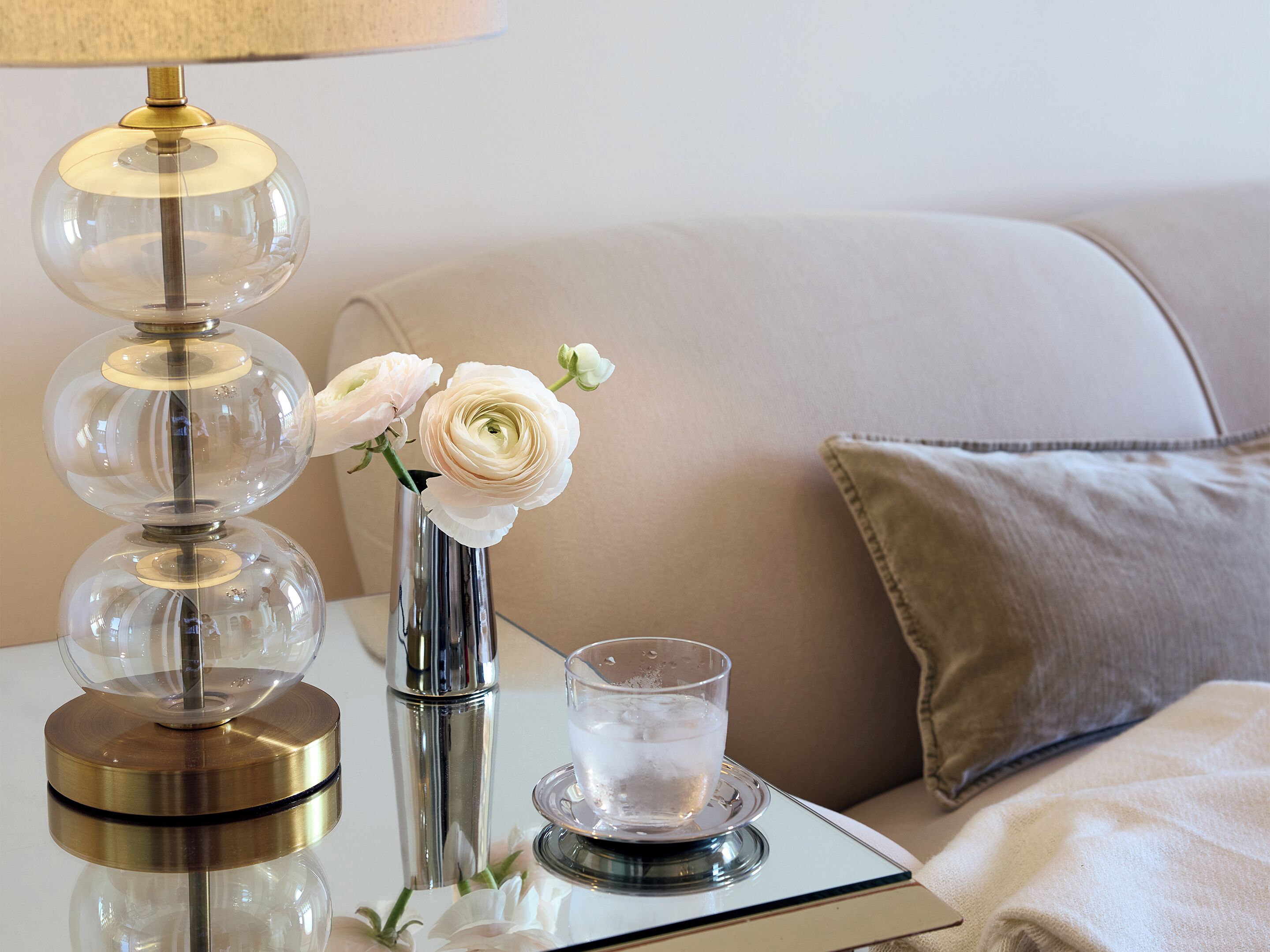 A bedside table with a lamp, a glass vase with flowers, and a glass of water.