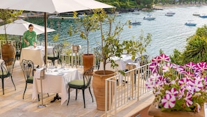 Un área de comedor al aire libre con mesas y sillas, con vista a una masa de agua y barcos.