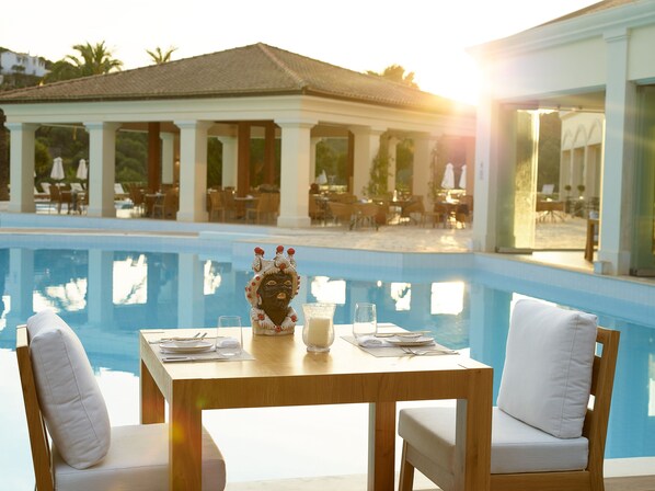 A dining table with chairs and a decorative centerpiece by a poolside. - Grecotel Eva Palace (Corfu)