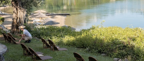A lakeside setting with lounge chairs and a tree, boats in the background, and a dock.