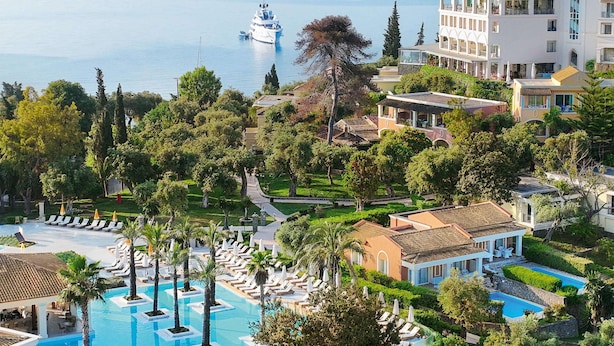 Un resort con una amplia zona de piscina, un yate amarrado cerca del agua y un edificio con varios balcones con vistas al mar.