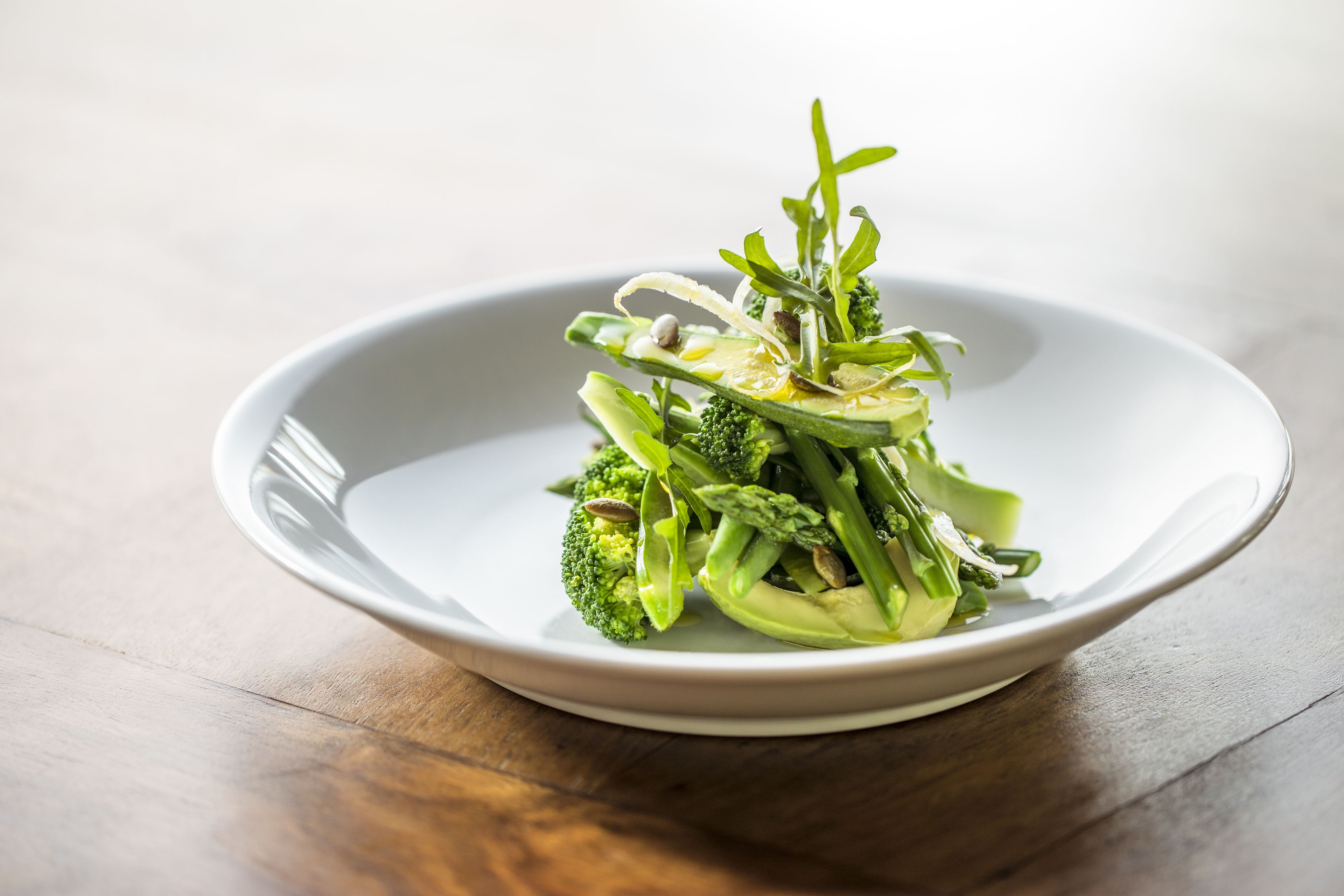 A white plate with a green vegetable dish on a wooden table.