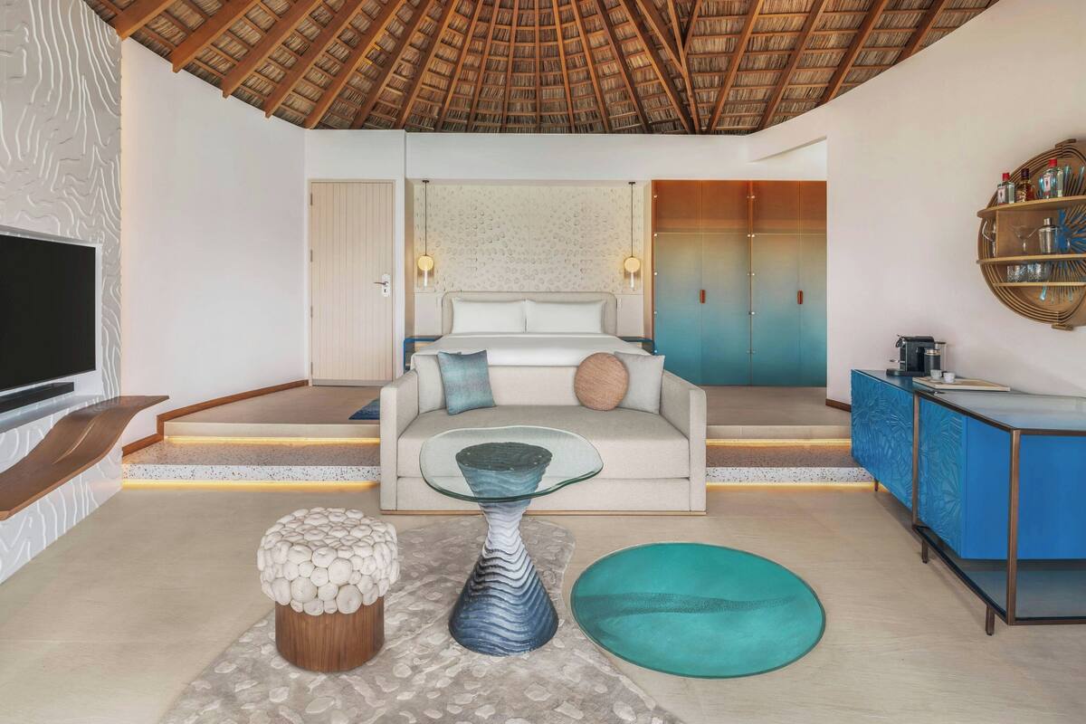 Una habitación de hotel moderna con una cama grande, un televisor, una mesa de centro de vidrio y un armario azul.