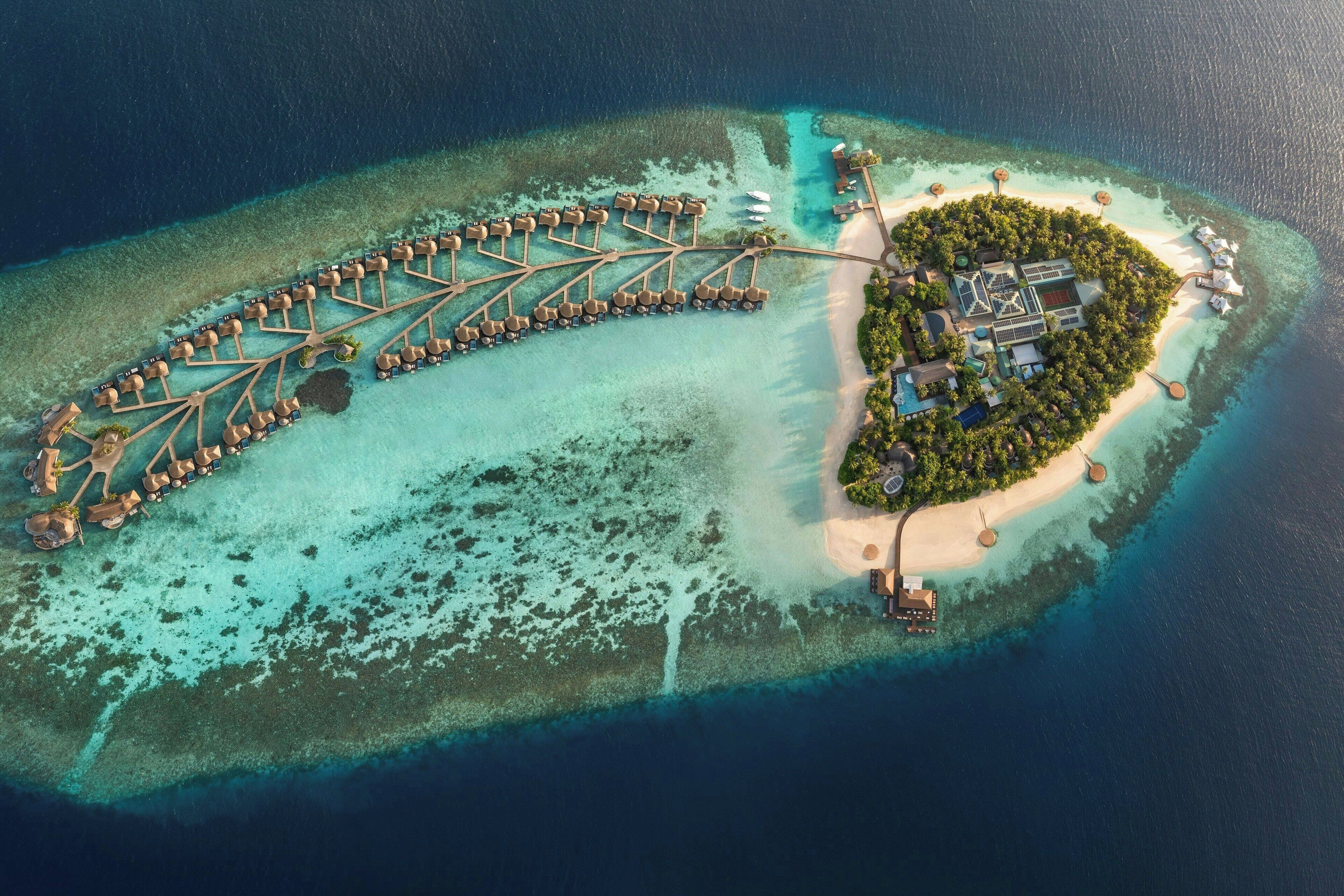 Eine Luftaufnahme einer Inselresort mit überwasser Bungalows, die durch Wege verbunden sind, einem zentralen Gebäude und einem Strandbereich.