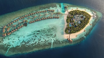 Eine Luftaufnahme einer Inselresort mit überwasser Bungalows, die durch Wege verbunden sind, einem zentralen Gebäude und einem Strandbereich.