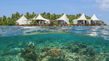 Een resort met bungalows boven het water, verbonden door een houten terras, omgeven door een tropisch landschap en helderblauw water.