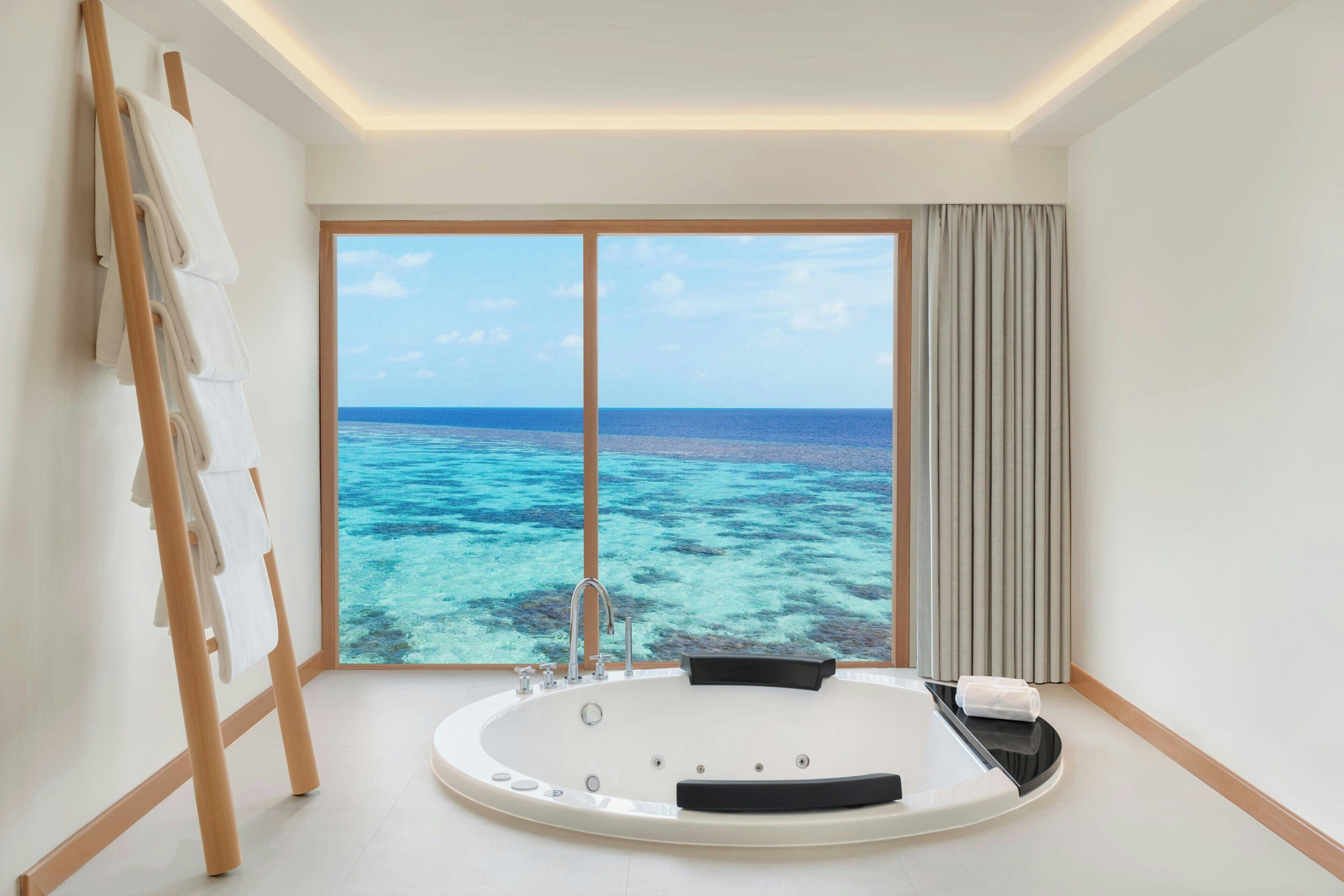A modern bathroom with a large bathtub, a wooden ladder, and a view of the ocean.