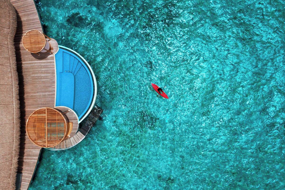 Vista aérea de un resort con una piscina azul cristalina, un kayak rojo y sillas de madera en terraza.
