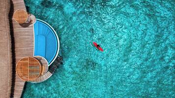 An aerial view of a resort with a clear blue pool, a red kayak, and wooden deck chairs.
