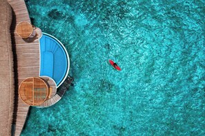 An aerial view of a resort with a clear blue pool, a red kayak, and wooden deck chairs. - W Maldives (Fesdu Island)