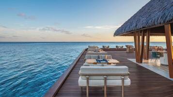 Una terraza de madera con asientos y una estructura de techo de paja con vista al mar.