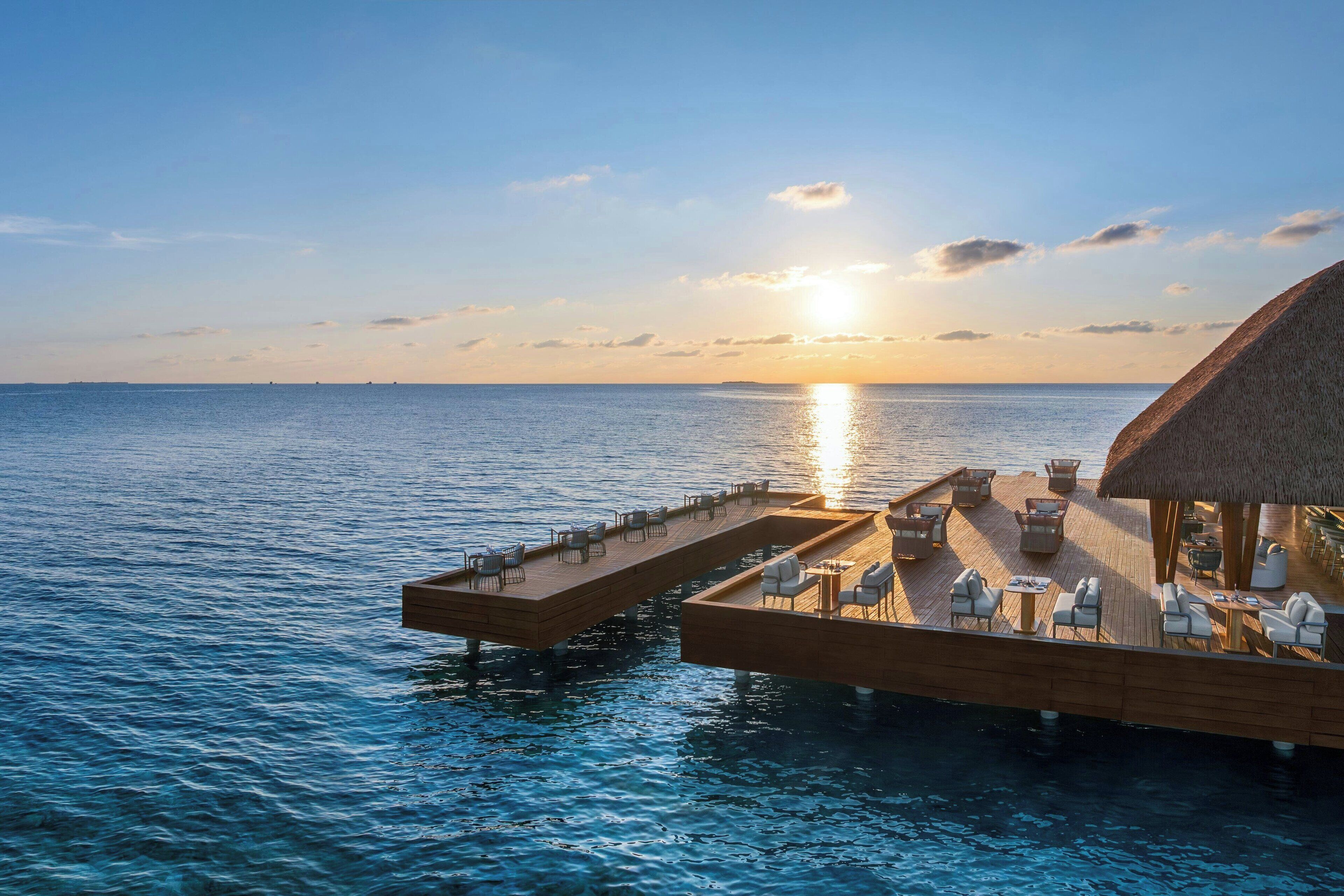 A wooden deck with outdoor seating overlooking the ocean at sunset.