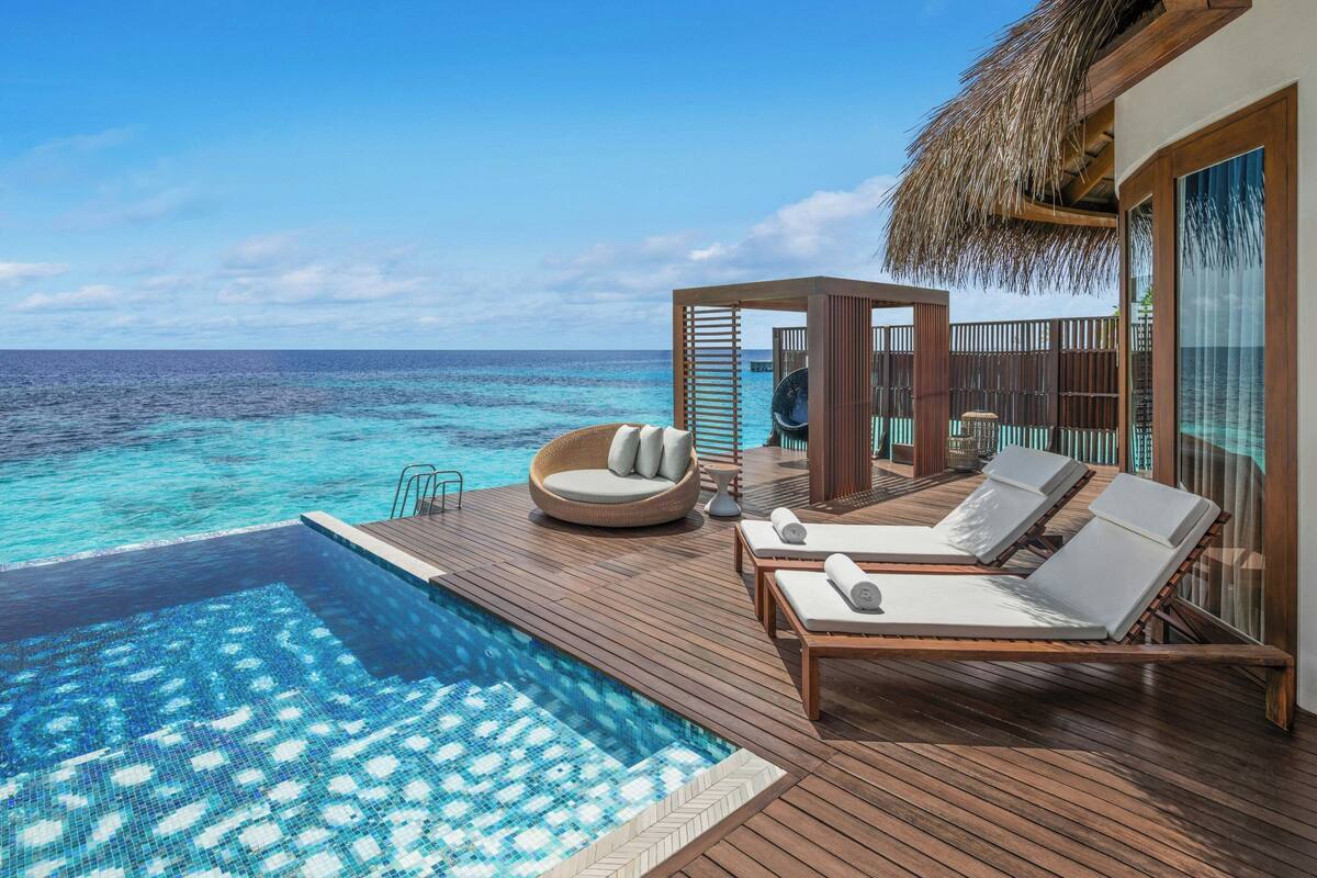 Una terraza de madera con piscina, sillas de descanso y una estructura con techo de paja.
