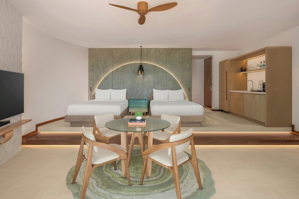 A modern living room with a sofa set, a dining table with chairs, a TV, and a kitchen area with cabinets.