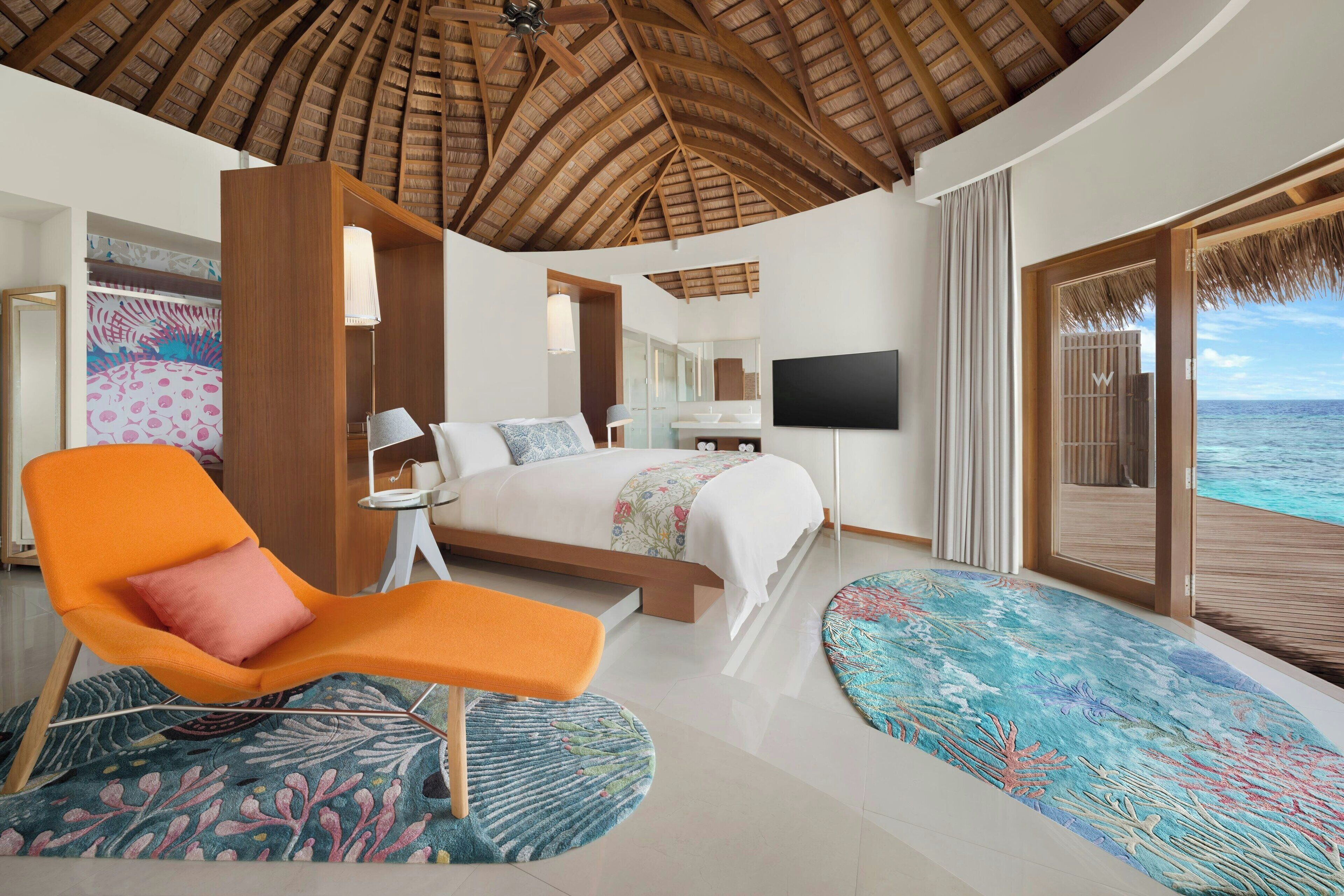 A bedroom with a bed, a TV, a chair, and a view of the ocean.