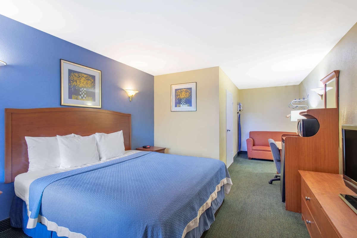 A hotel room with a large bed, a desk with a computer, a TV, and two framed pictures on the wall.