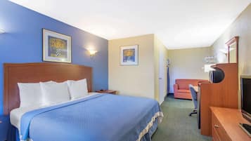 A hotel room with a large bed, a desk with a computer, a TV, and two framed pictures on the wall.